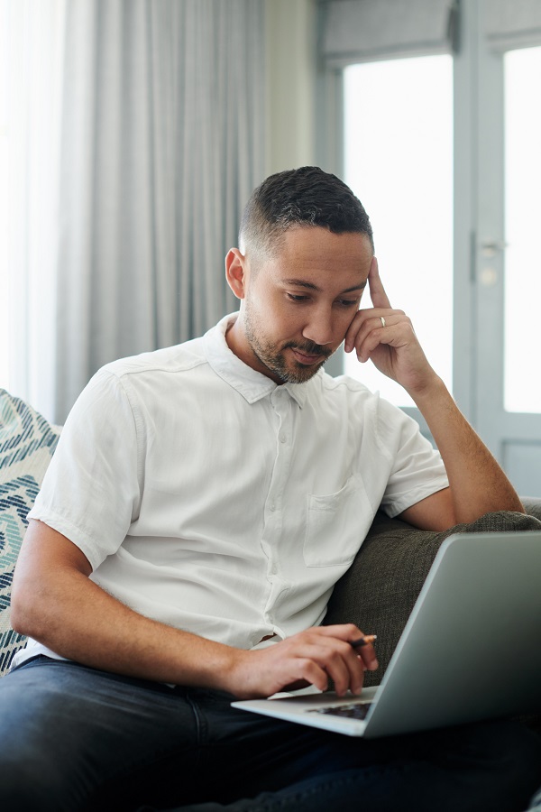 Shot Of A Handsome Young Man Sitting Alone On His Sofa At Home And Looking Contemplative While Working From Home